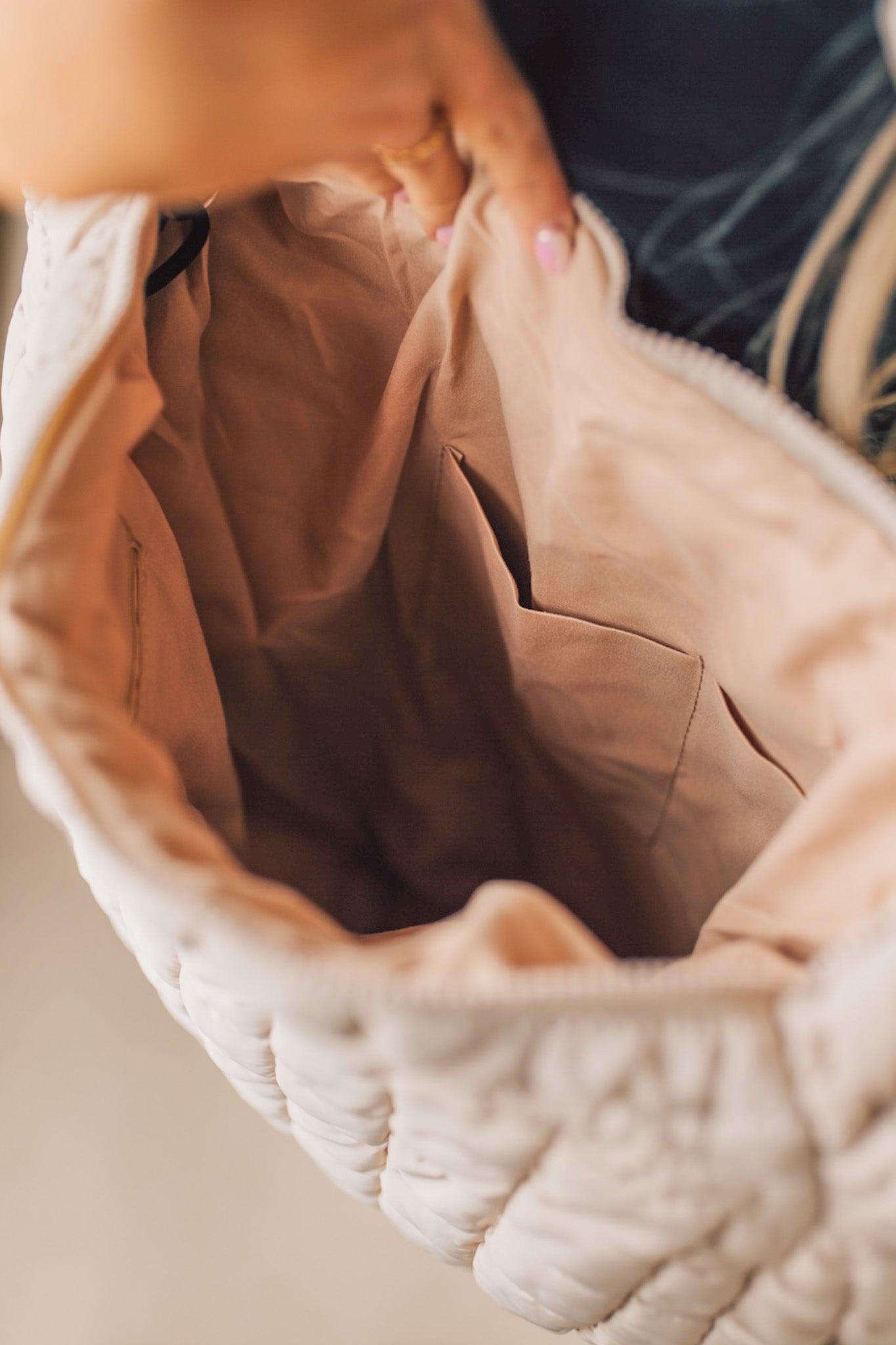 Blonde woman holding an almond color oversized tote with nylon quilted exterior.