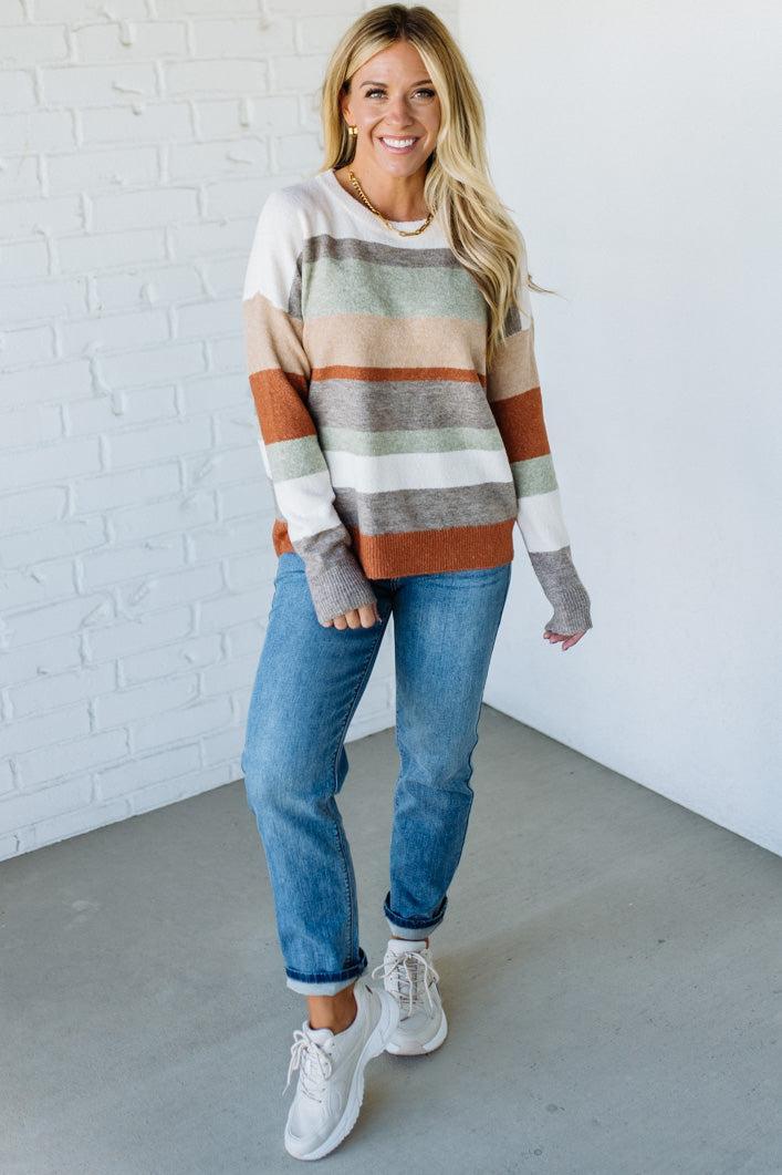 Woman wearing a striped sweater and jeans standing against a white brick wall.