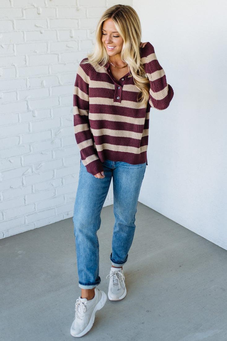 Woman wearing a striped sweater and jeans against a white brick wall.
