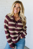 Woman wearing a maroon and beige striped sweater against a white brick wall.