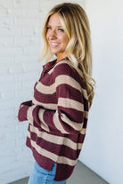 Woman wearing a burgundy and beige striped sweater against a white brick wall.