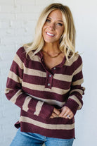 Woman wearing a maroon and beige striped sweater against a white brick wall.