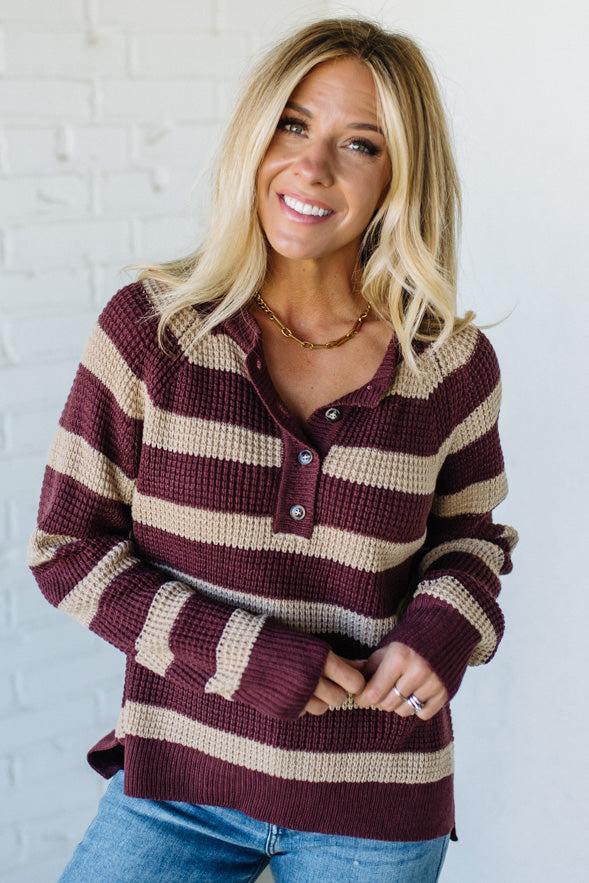 Woman wearing a maroon and beige striped sweater against a white brick wall.