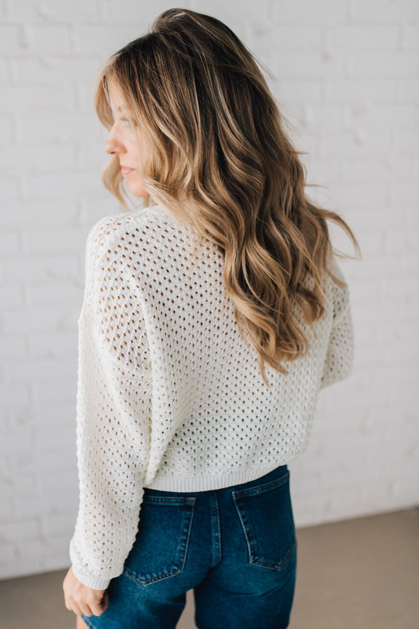 Blonde woman wearing a loose knit low gauze white sweater with drop shoulder and woven American flag at center front.