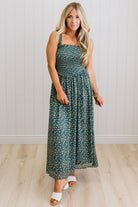 Woman wearing a green floral dress standing against a white paneled wall.