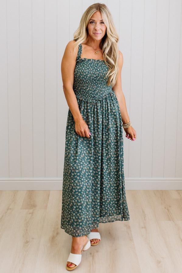 Woman wearing a green floral dress standing against a white paneled wall.
