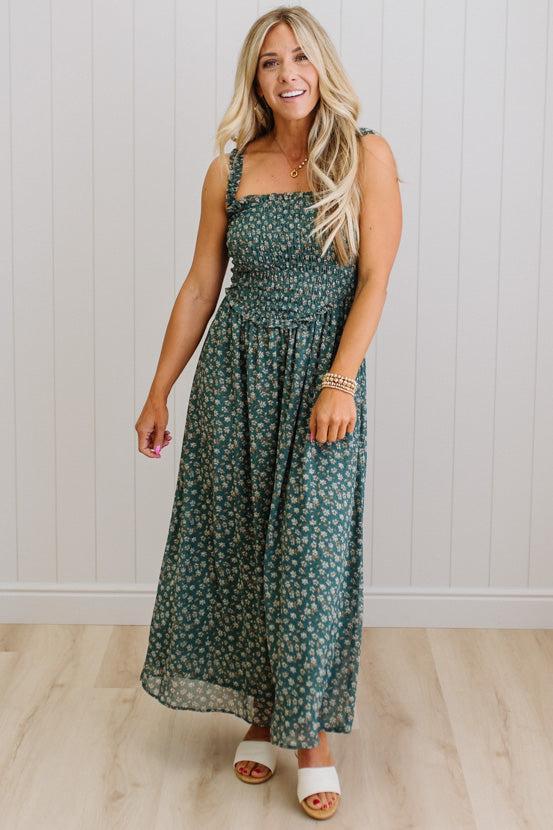 Woman wearing a green floral dress against a white paneled wall.