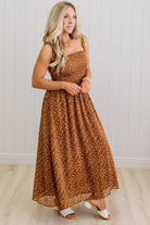 Woman wearing a brown floral dress standing against a white wall.