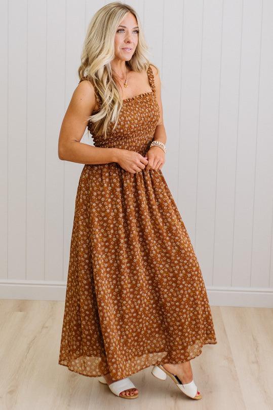 Woman wearing a brown floral dress standing against a white wall.
