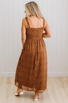 Woman wearing a brown floral dress standing against a white wall.