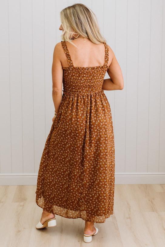Woman wearing a brown floral dress standing against a white wall.
