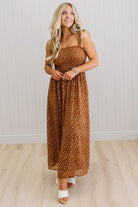 Woman wearing a brown floral dress standing against a white paneled wall.
