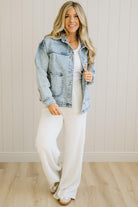 Woman wearing a denim jacket over a white top and pants in a neutral setting