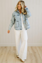 Woman wearing a light blue denim jacket over a white top and pants, standing against a plain background.