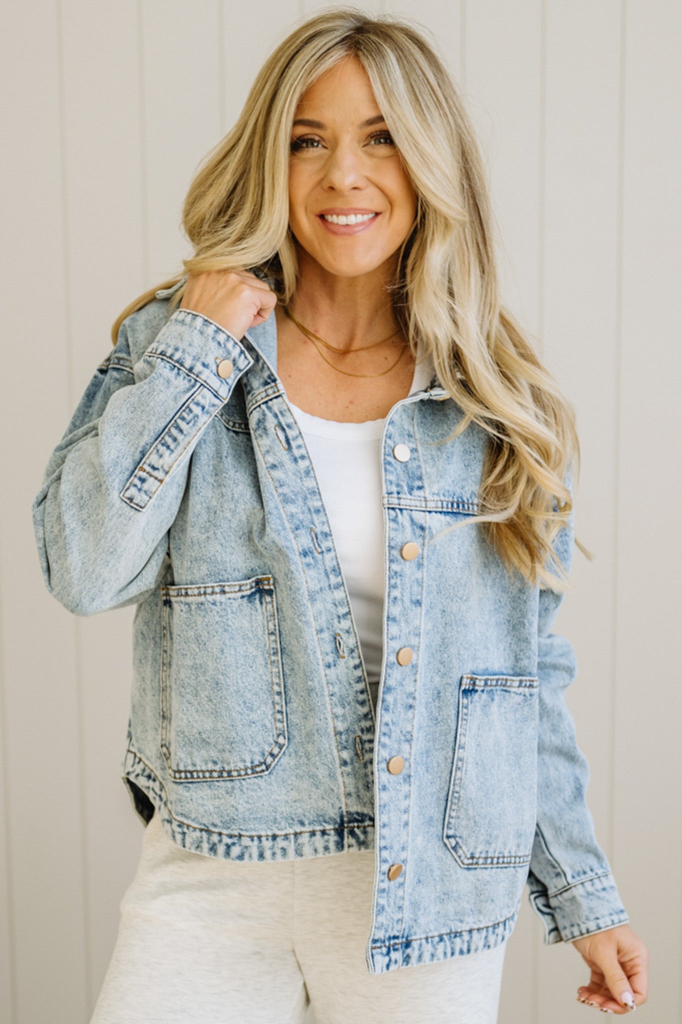 Woman wearing a light blue denim jacket over a white top against a neutral background