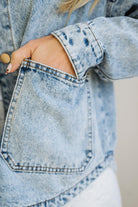 Close-up of a person wearing a light blue denim jacket with a pocket.