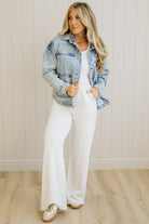 Woman wearing a denim jacket over a white top and pants in a neutral setting
