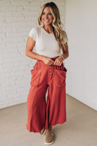 Woman wearing a white top and red pants with a white brick wall background