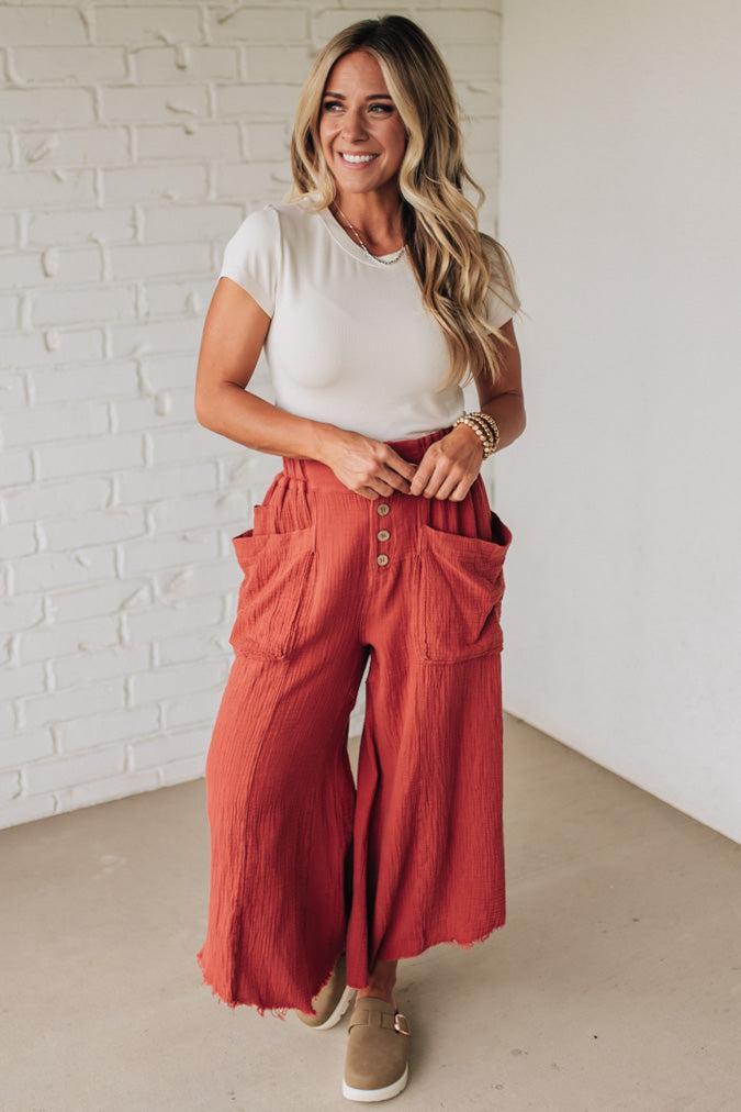Woman wearing a white top and red pants with a white brick wall background