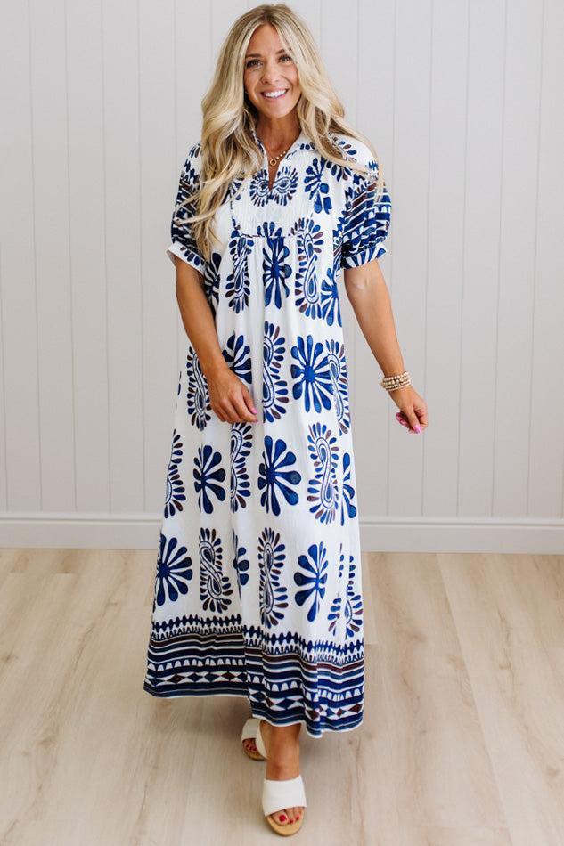Woman wearing a blue and white patterned dress standing against a white paneled wall.