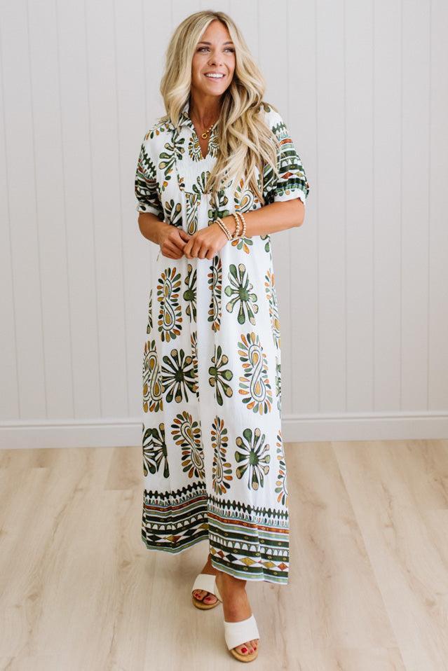 Woman wearing a patterned dress standing against a white wall.