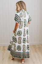 Woman wearing a patterned dress standing in a room with wooden flooring and white walls.