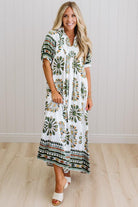 Woman wearing a long, patterned dress standing against a white wall.