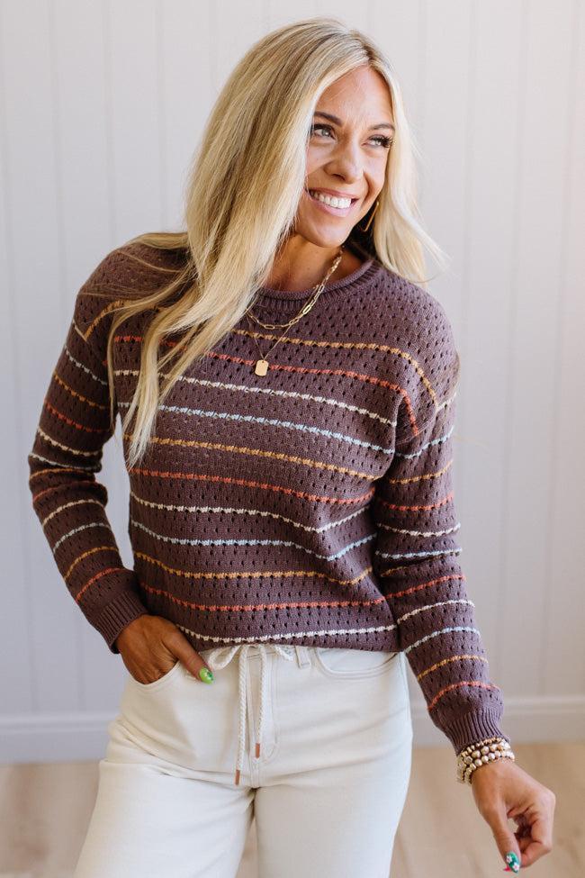 Blonde woman wearing an all over perforated mocha brown sweater with thin horizontal multi color stripes, a rolled neckline and ribbed cuff.