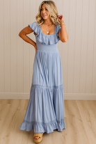 Woman wearing a blue dress standing against a beige wall.