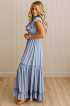 Woman wearing a light blue dress with ruffled details in a room with wooden flooring and a neutral wall.