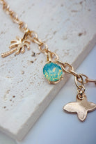 Gold necklace with a geen-blue gemstone and whale charm on a light stone surface