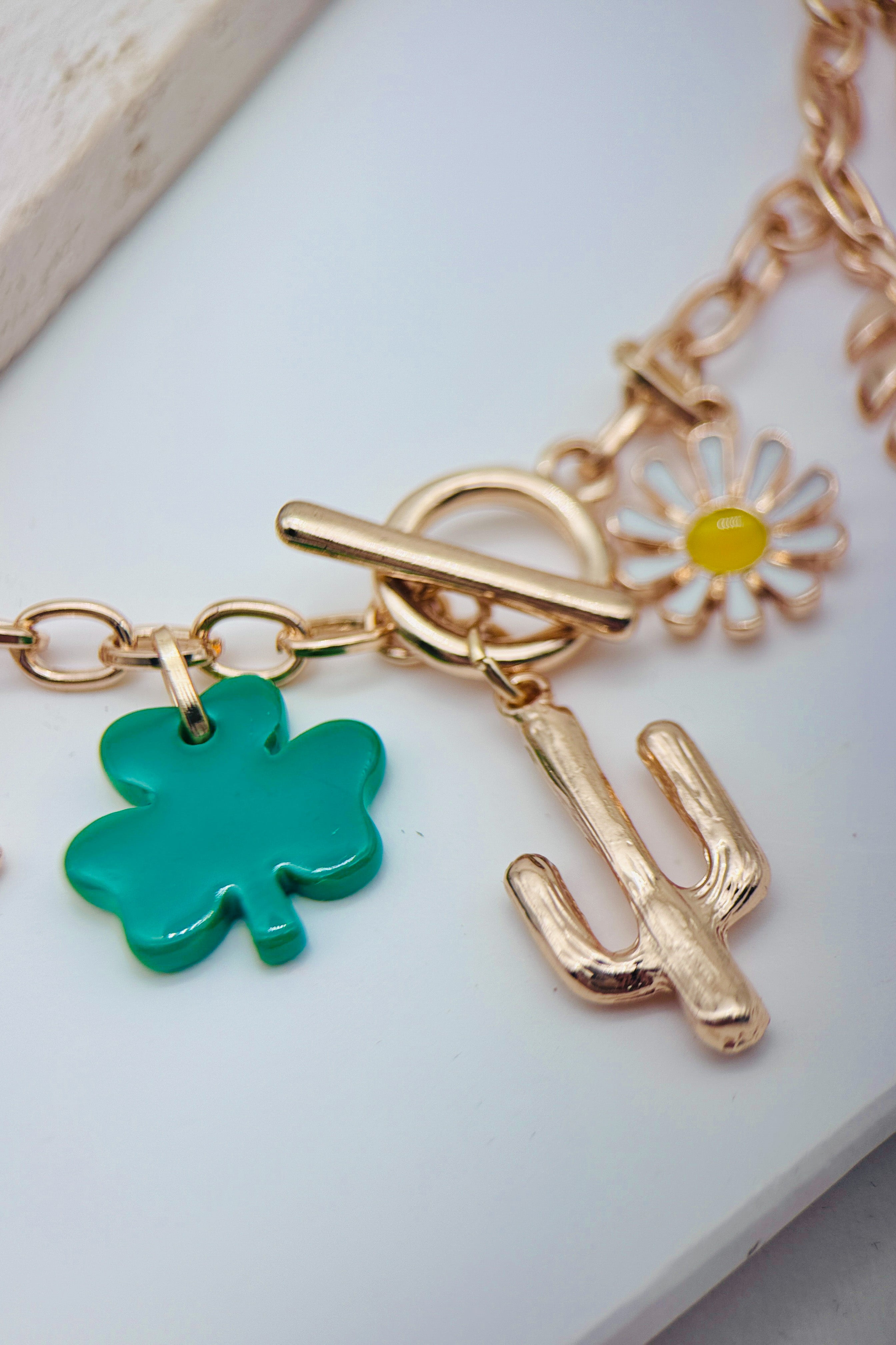 Gold necklace with charms including a green clover, yellow flower, and gold cactus on a white surface.