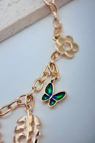 Gold necklace with butterfly and leaf charms on a light background