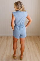 Woman wearing a light blue romper standing on a wooden floor with a neutral wall background