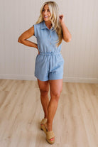 Woman wearing a light blue romper standing on a wooden floor with a white wall background