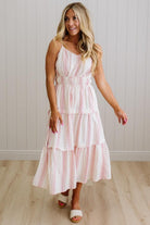 Woman wearing a white dress with red stripes in a room with wooden flooring and a white wall.