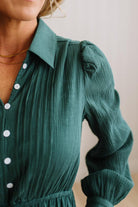 Close-up of a woman wearing a dark green crinkle-textured blouse with white buttons, featuring a pointed collar and puffed long sleeves.