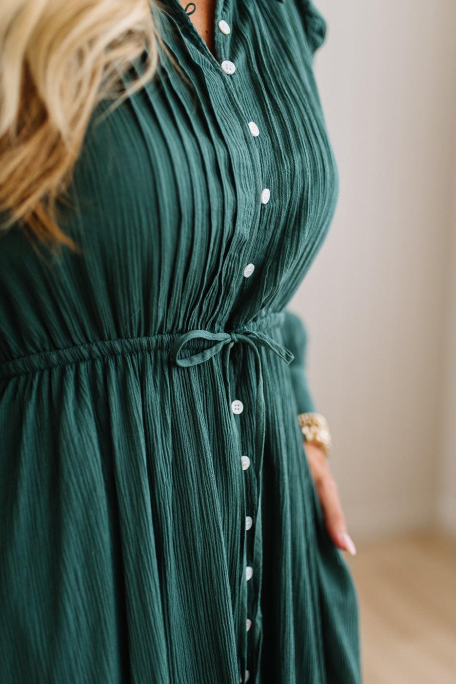 Close-up of a woman wearing a dark green crinkle-textured blouse with white buttons, featuring a tie waist.