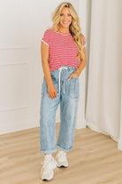 Woman wearing a red and white striped shirt, blue jeans, and white sneakers indoors.