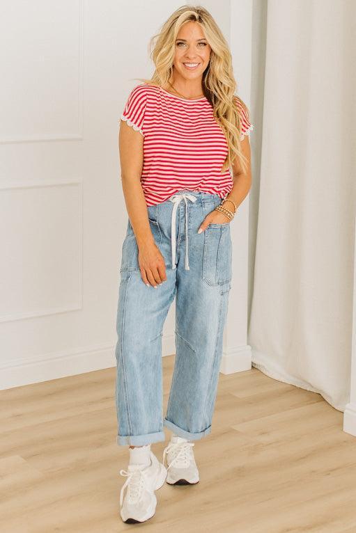 Woman wearing a red and white striped shirt, blue jeans, and white sneakers indoors.