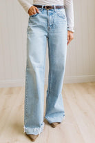 Woman wearing a gray t-shirt and light blue jeans standing on a wooden floor with a white wall background.