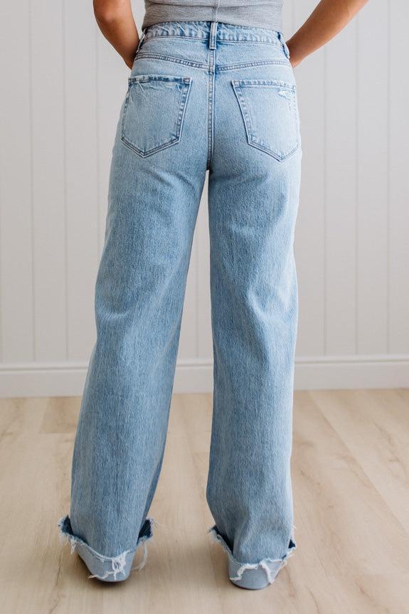 Light blue jeans worn by a person on a light wooden floor with a white paneled wall background