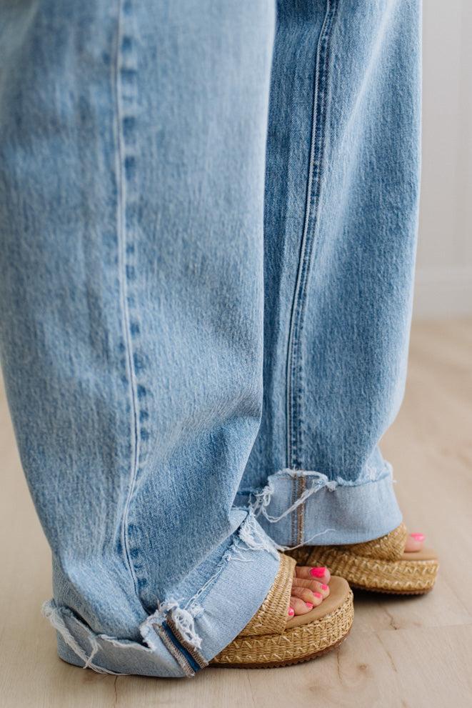 Close-up of rolled-up blue jeans with sandals on a neutral background