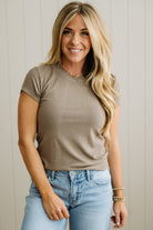 Woman wearing a brown t-shirt and blue jeans against a neutral background