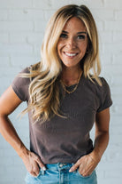 Woman wearing a brown t-shirt and blue jeans against a white brick wall.