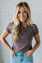 Woman wearing a brown t-shirt and blue jeans against a white brick wall.