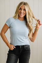 Woman wearing a light blue t-shirt and black jeans against a white wall.