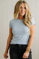 Woman wearing a light blue t-shirt and black pants against a neutral background