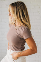 Woman wearing a brown t-shirt and white pants against a light gray background