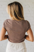 Person wearing a brown t-shirt and beige pants against a white brick wall.